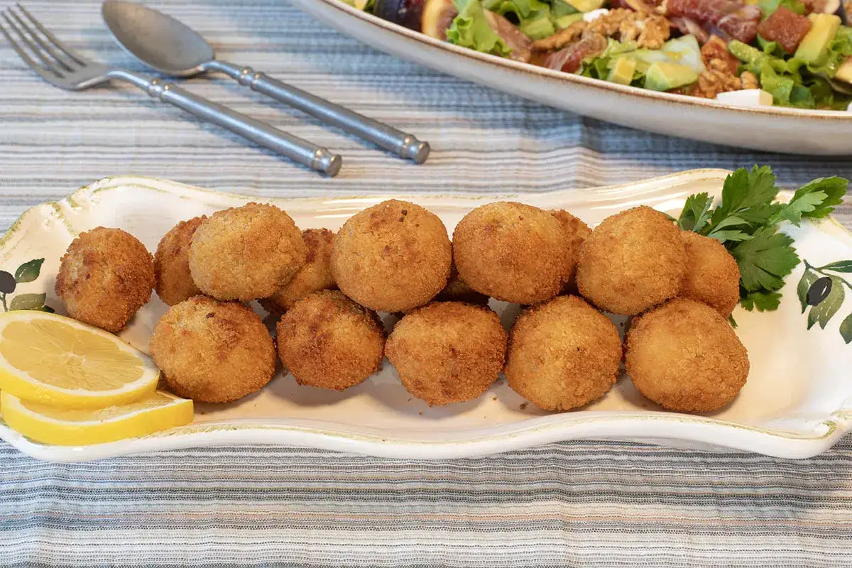 Croquetas de pollo doradas y crujientes en una bandeja decorada, acompa&ntilde;adas de rodajas de lim&oacute;n y perejil.