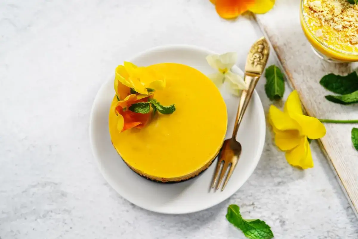 Delicioso mousse de mango, decorado con flores amarillas y menta. Un postre vibrante y refrescante.