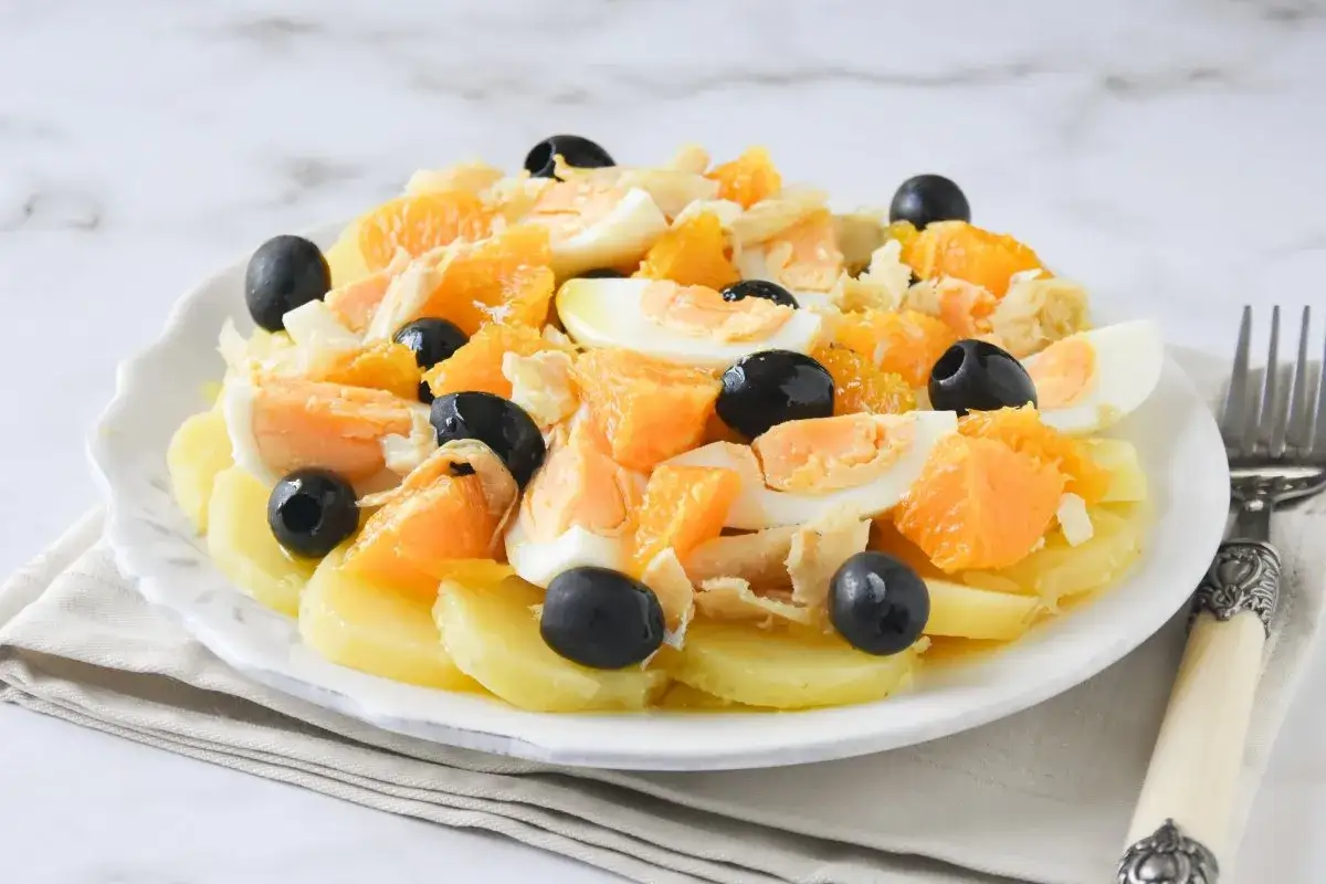 Deliciosa ensalada de bacalao con patatas, huevo duro, naranja y aceitunas negras. Un plato fresco y lleno de sabor.
