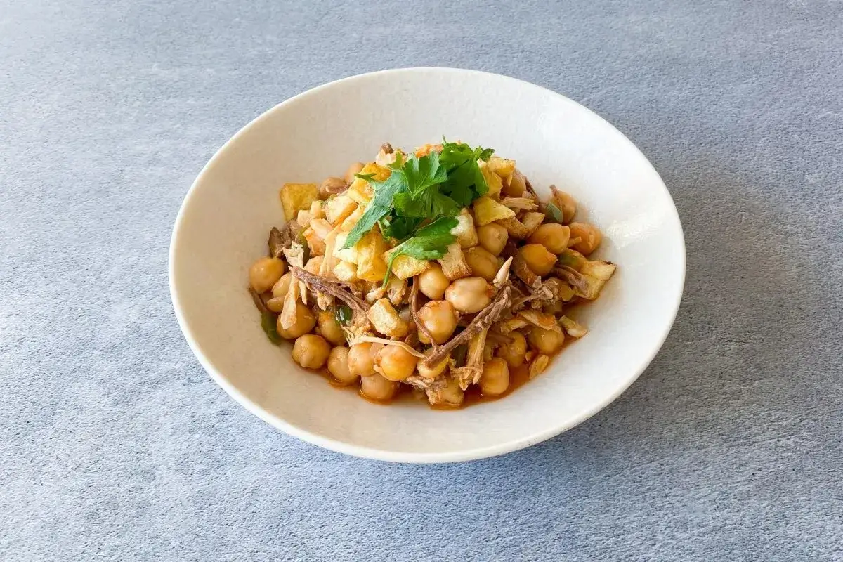 Un plato de ropa vieja canaria, con garbanzos, carne deshebrada y patatas fritas, adornado con perejil fresco.