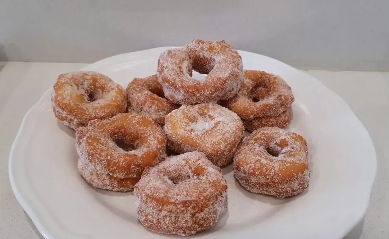 Roscos de Semana Santa espolvoreados con az&uacute;car, apilados en un plato blanco.