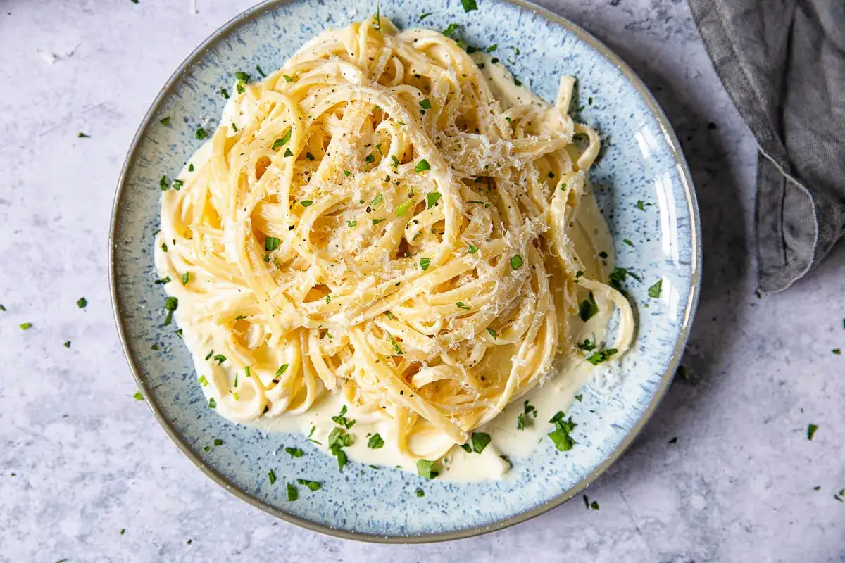 Un plato de espaguetis con nata, cubierto de queso rallado y perejil picado.