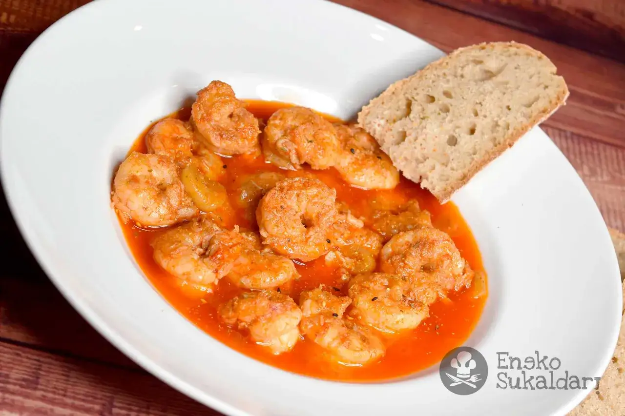 Un plato de gambas al ajillo en una cazuela blanca, con un trozo de pan rústico.