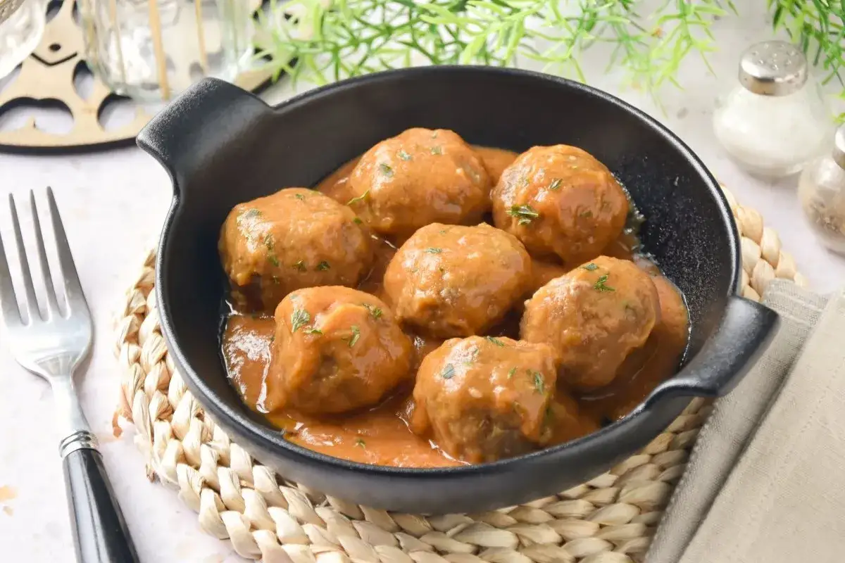 Albondigas en salsa casera, servidas en una cazuela negra sobre una esterilla de mimbre. Un plato reconfortante listo para disfrutar.