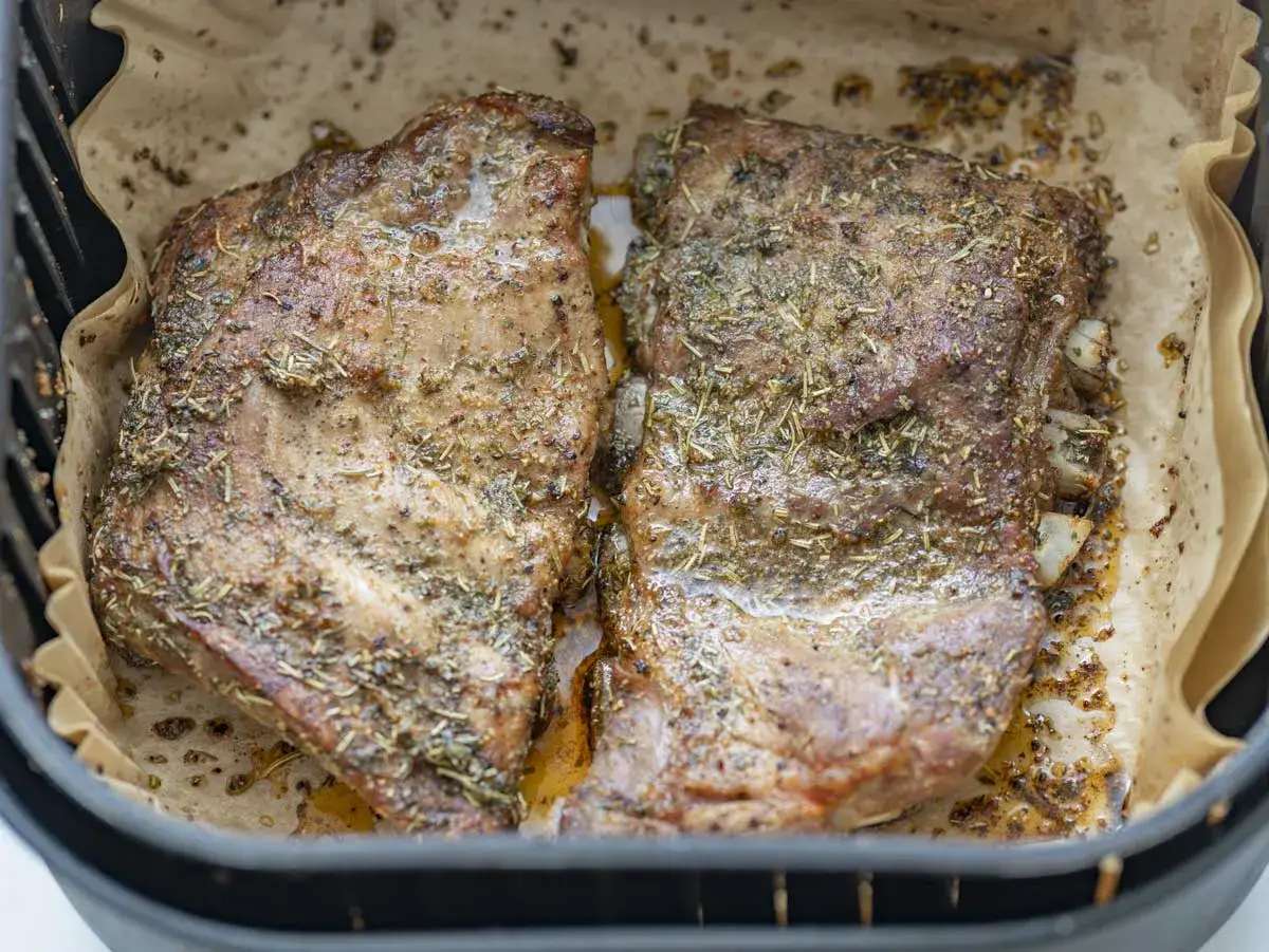 Dos costillas de cerdo jugosas y doradas, sazonadas con hierbas, listas para disfrutar tras su paso por la freidora de aire.