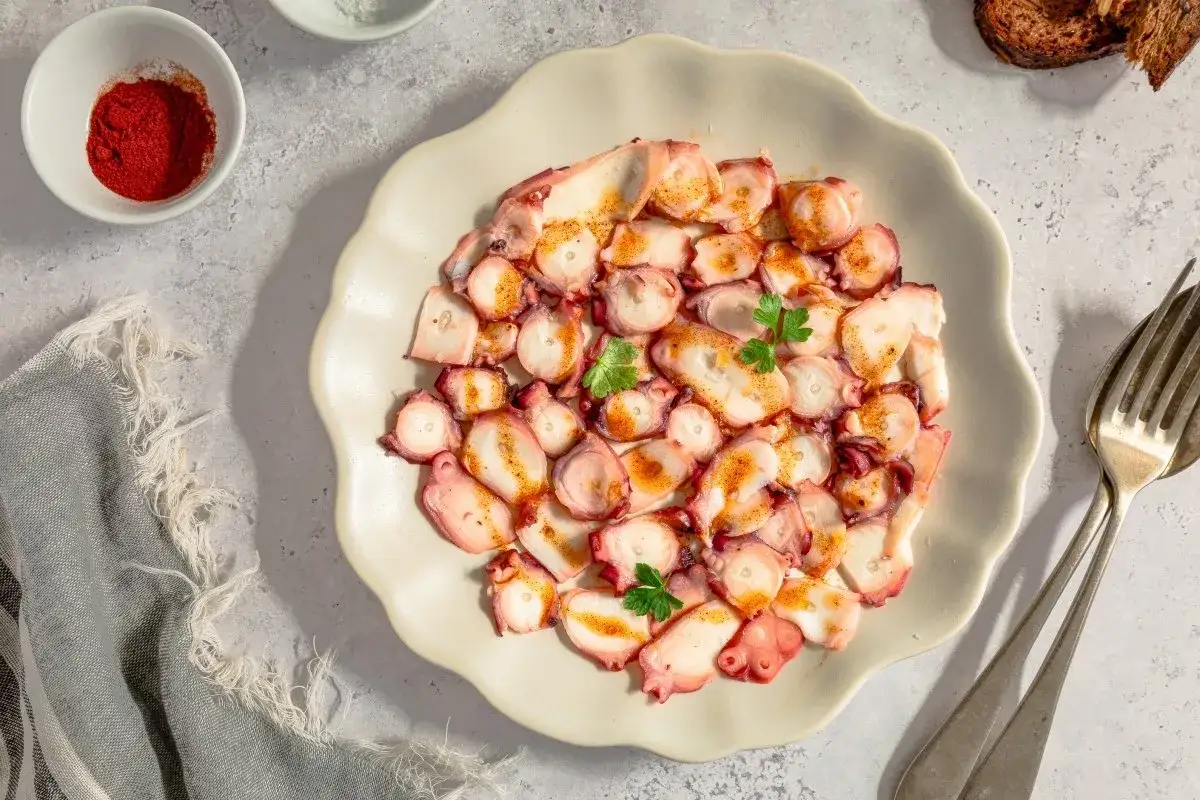 Delicioso carpaccio de pulpo, finas l&aacute;minas con piment&oacute;n y perejil, servido en plato blanco.