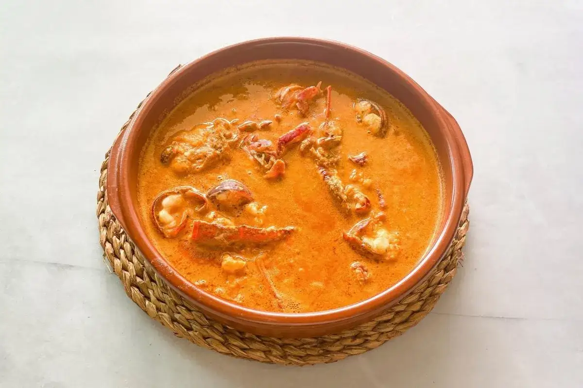 Caldereta de langosta, un plato marinero reconfortante con trozos de langosta en una salsa cremosa y anaranjada, servido en cazuela de barro.