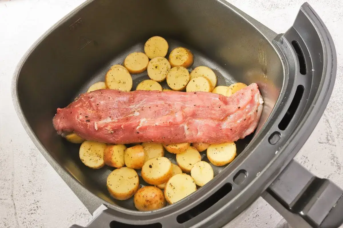 Solomillo de cerdo crudo con patatas cortadas en rodajas, listo para cocinar en la freidora de aire.