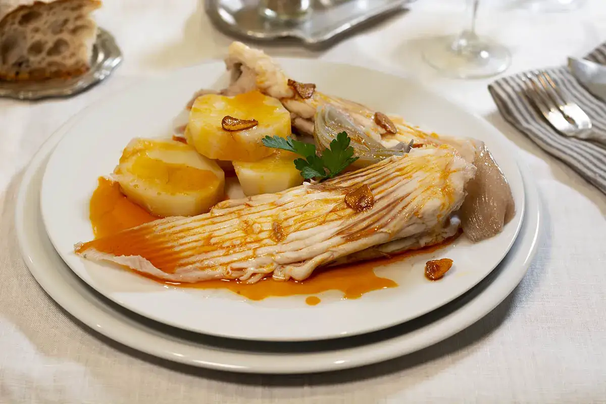 Raya a la gallega con patatas, ajo frito y perejil. Un plato tradicional gallego servido en un plato blanco.