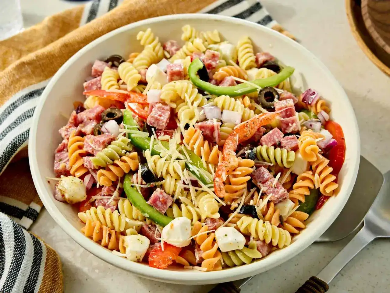 Ensalada de pasta colorida con salami, queso mozzarella, aceitunas, pimientos y cebolla roja, bañada en una deliciosa salsa para ensalada de pasta.