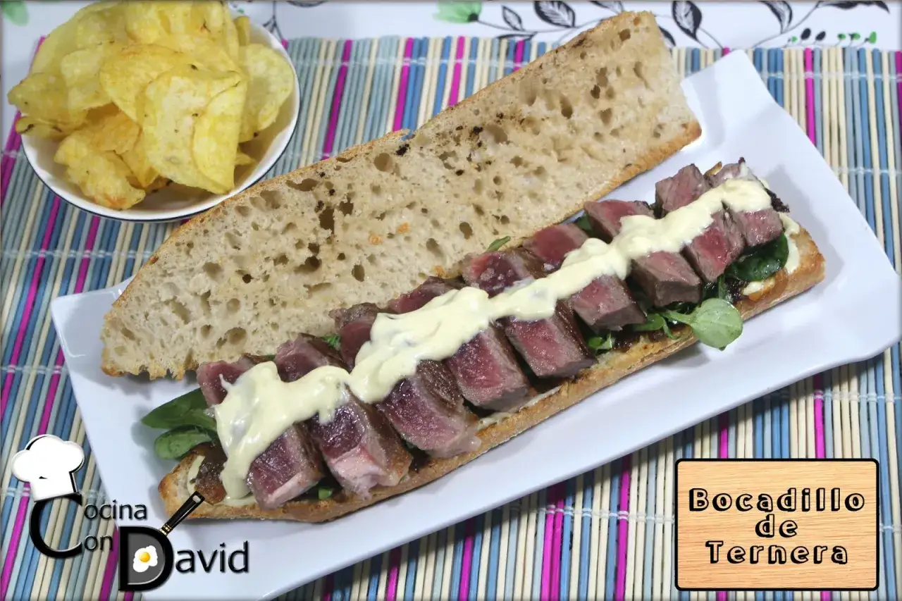 Un delicioso bocadillo de ternera jugosa, servido en pan r&uacute;stico con salsa cremosa y acompa&ntilde;ado de patatas fritas.