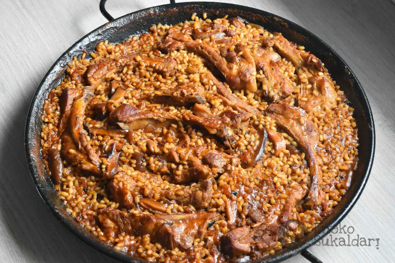 Arroz con costillas y champi&ntilde;ones, un plato reconfortante y lleno de sabor, servido en una paellera.