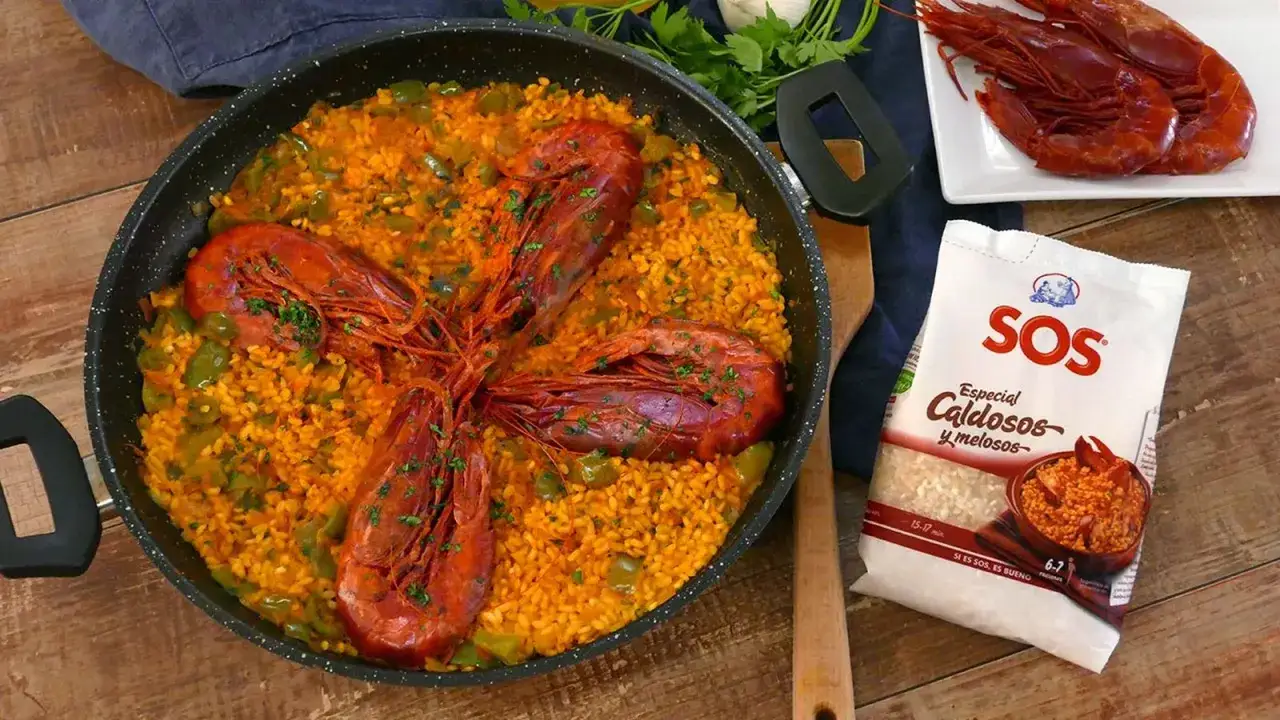 Arroz con carabineros en paellera, con pimientos verdes y perejil picado. A un lado, carabineros frescos y un paquete de arroz SOS.
