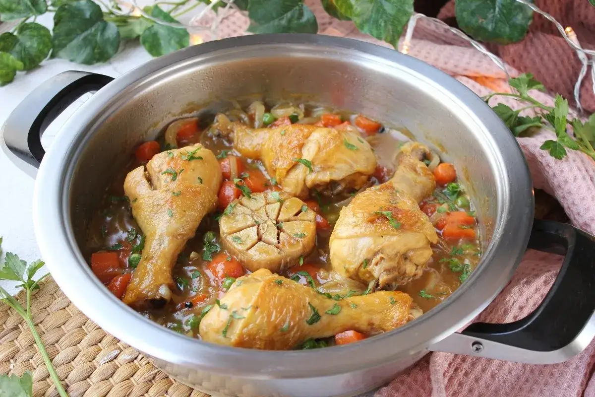 Muslos de pollo a la cerveza, tiernos y dorados, cocinados con zanahorias, guisantes y una cabeza de ajo entera en una rica salsa.