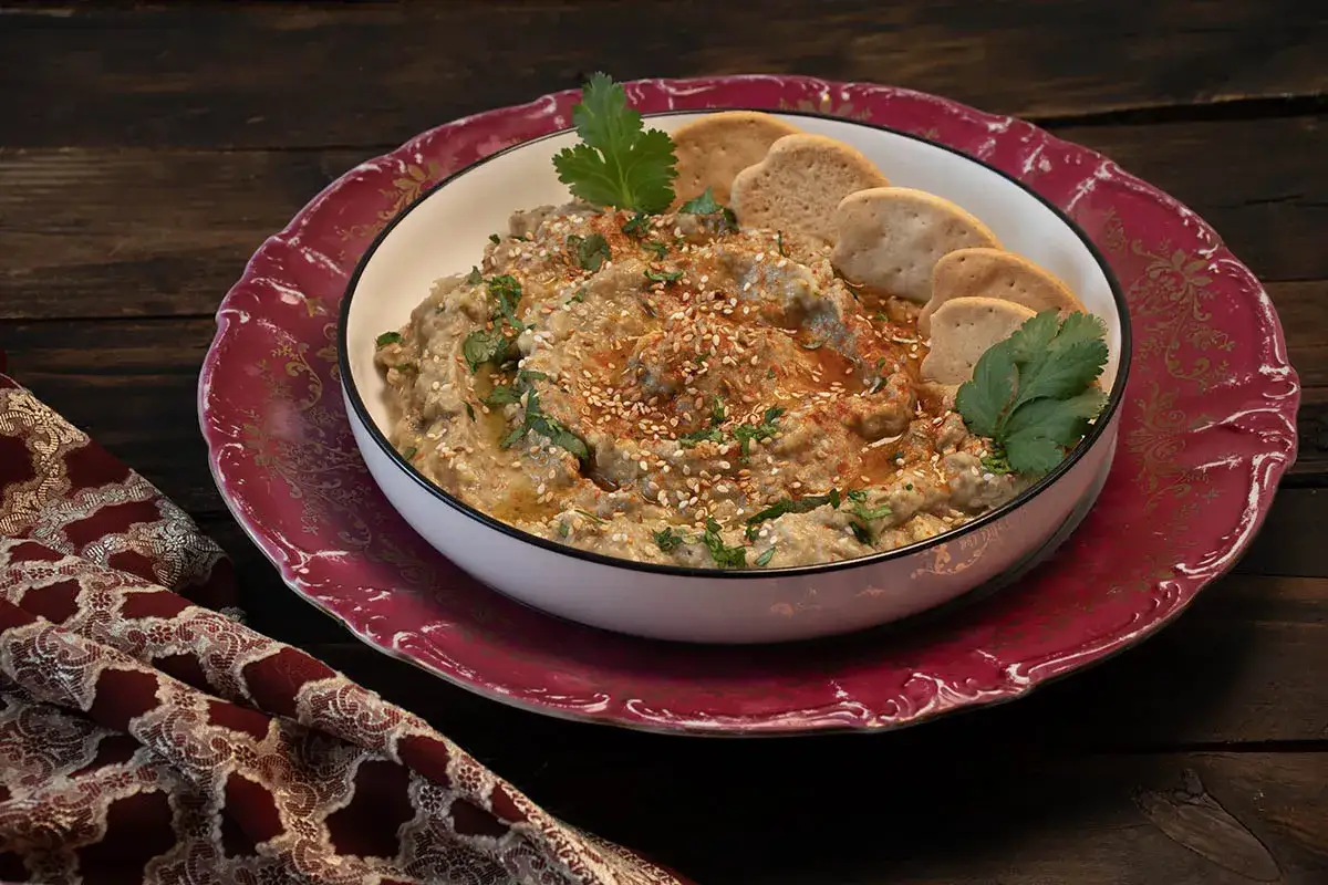 Un cremoso hummus de berenjena, espolvoreado con s&eacute;samo y perejil, servido con galletas.