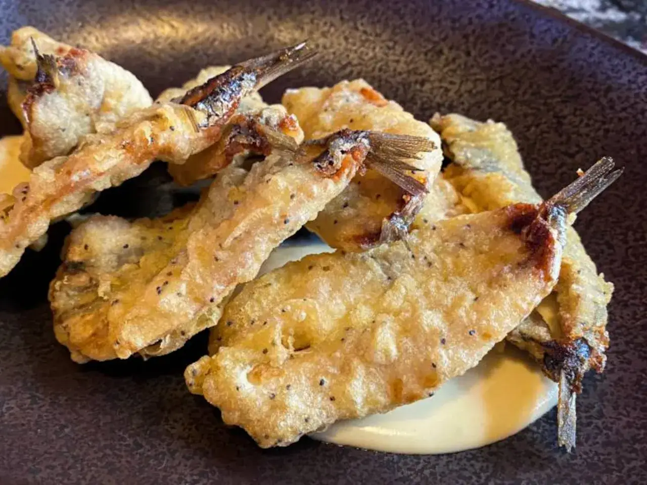 Boquerones a la andaluza crujientes y dorados, servidos sobre una base cremosa.