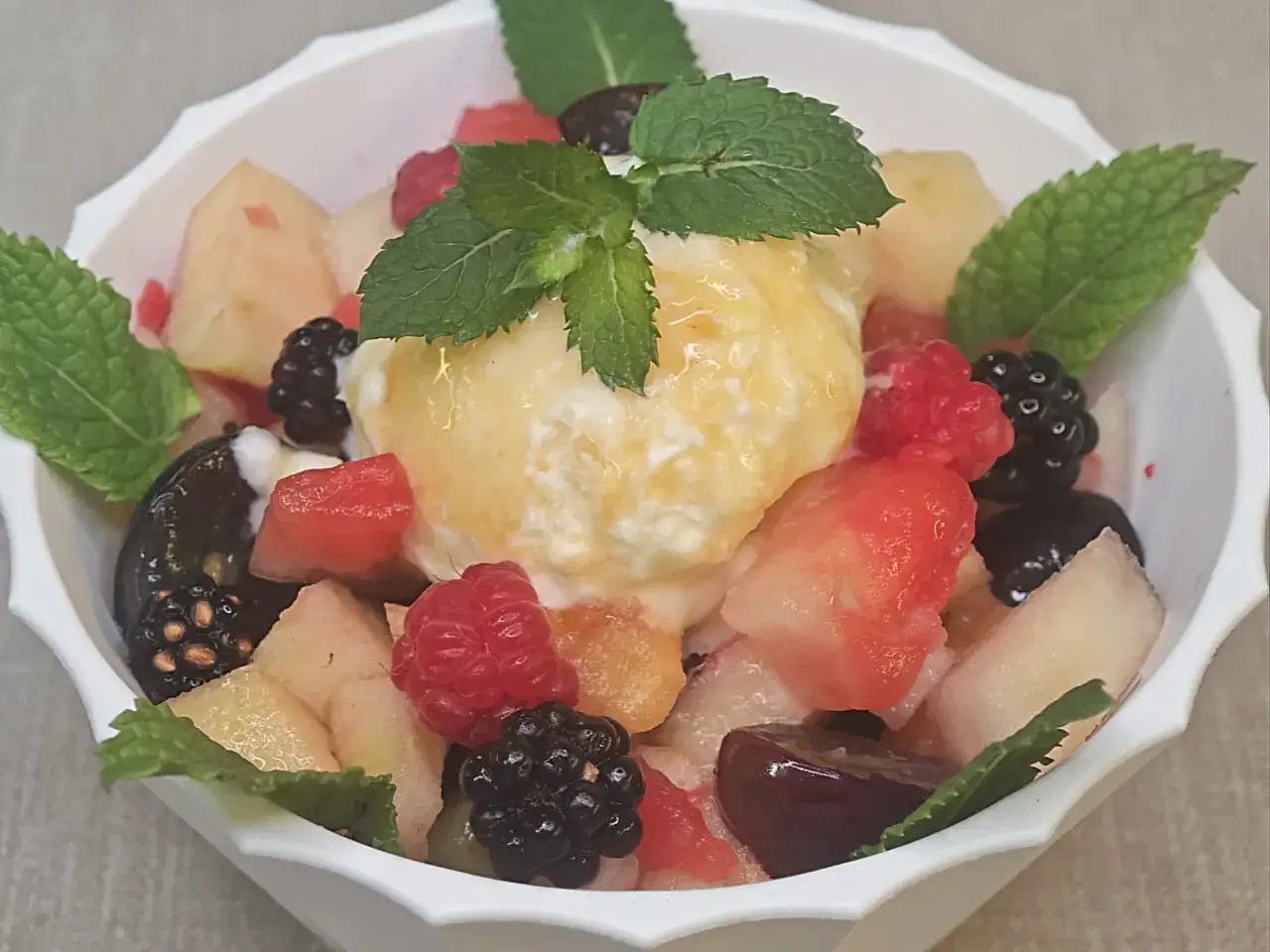 Deliciosa macedonia de frutas con helado de vainilla, frambuesas, moras, melocot&oacute;n y menta.
