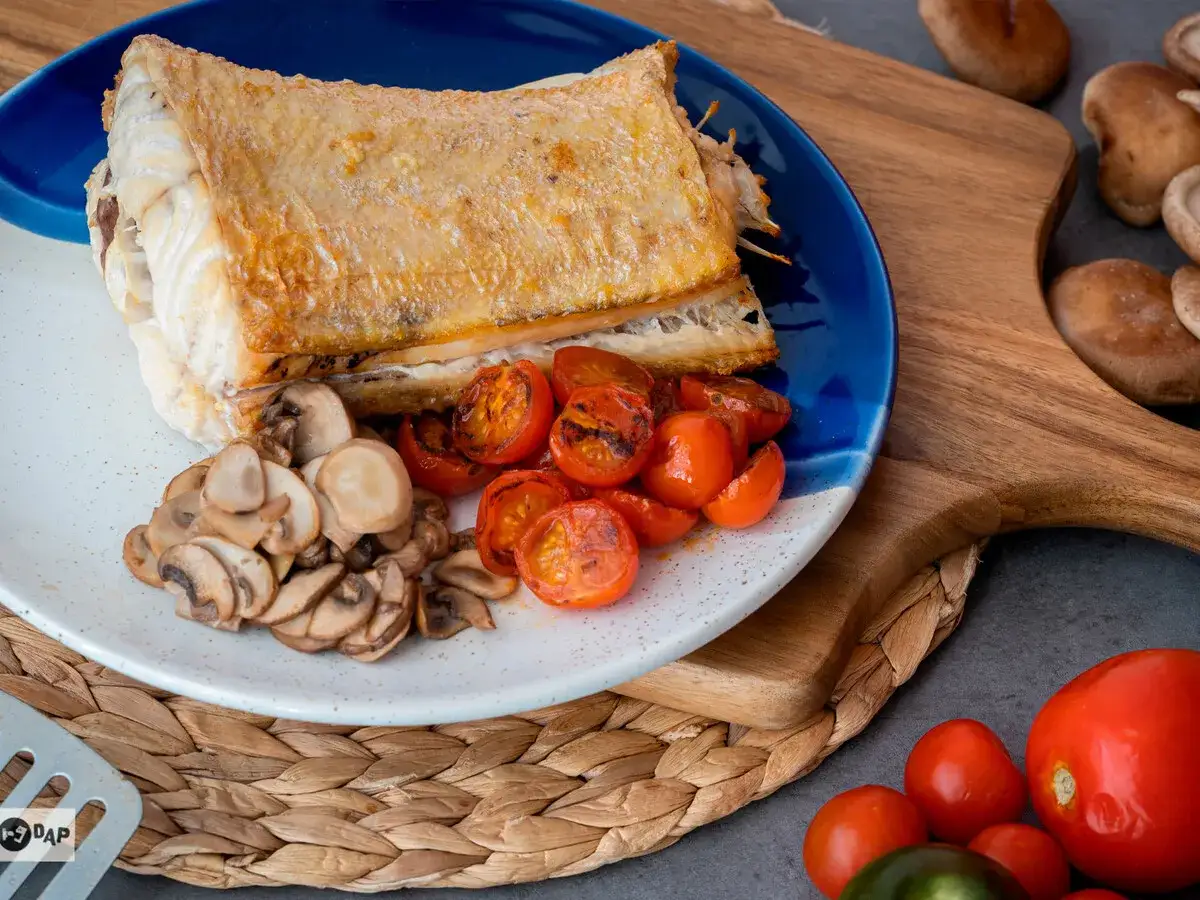 Pescado rosado al horno con champi&ntilde;ones y tomates cherry asados, servido en un plato azul y blanco.