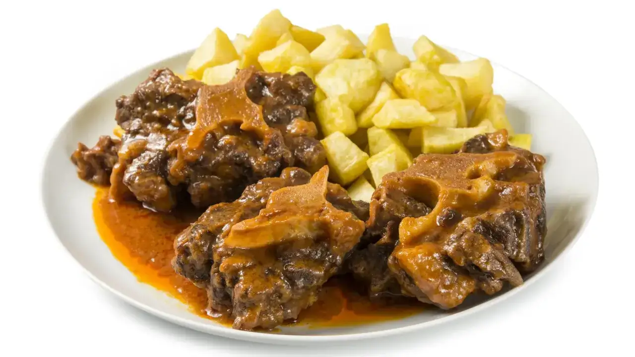 Plato de rabo de ternera estofado en salsa, acompa&ntilde;ado de patatas fritas doradas.
