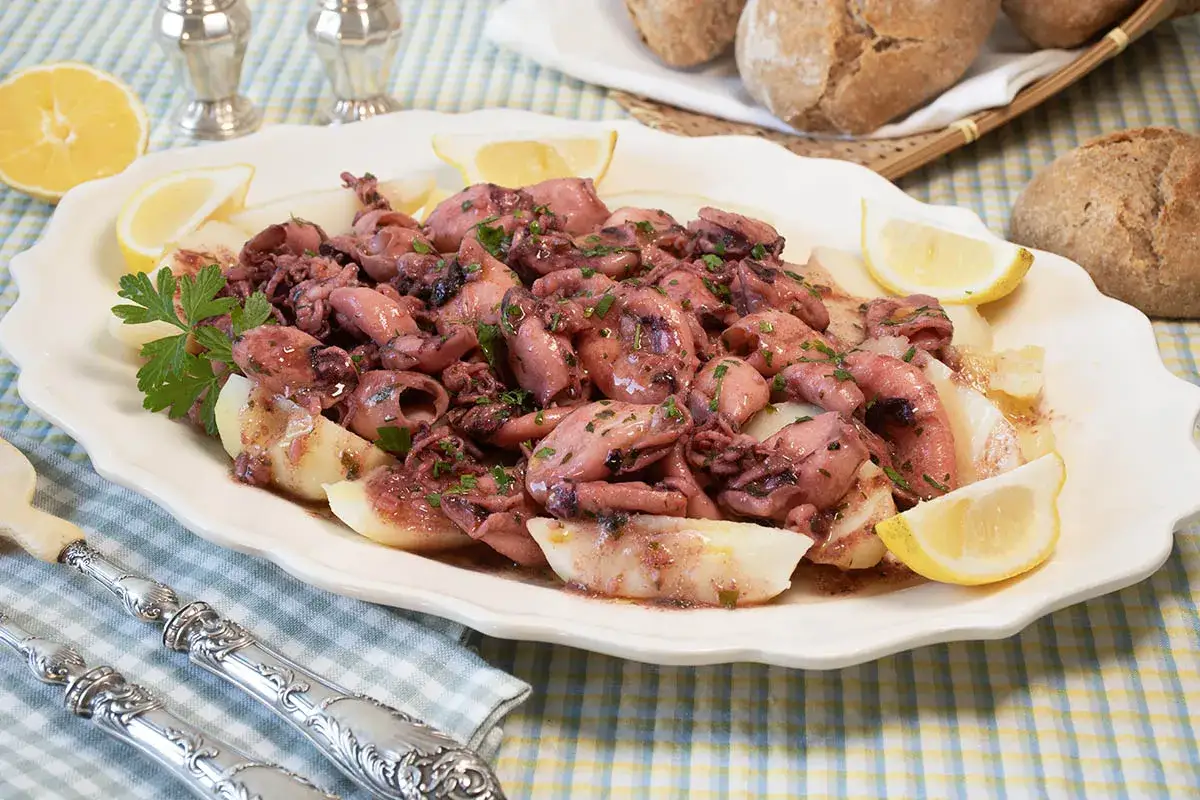 Chipirones a la plancha servidos en plato blanco con patatas y lim&oacute;n. Un plato delicioso y fresco.