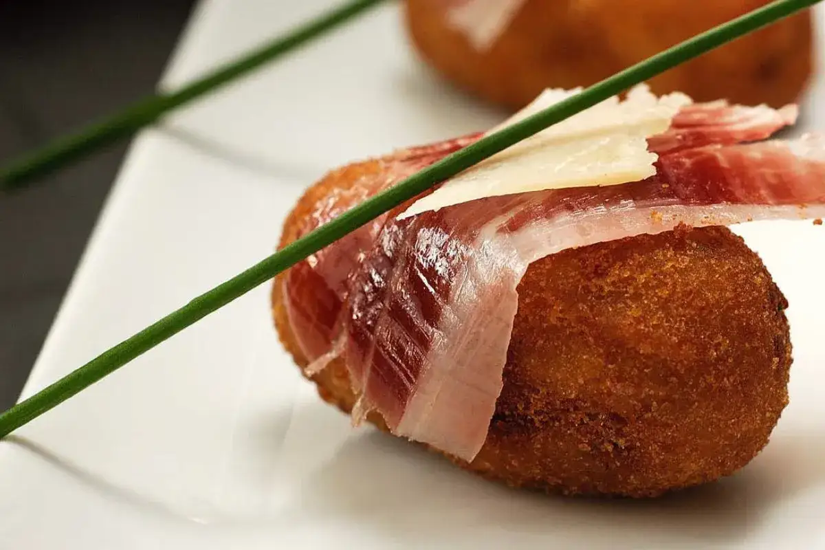 Croquetas de jam&oacute;n doradas, envueltas en jam&oacute;n serrano y coronadas con una lasca de queso.