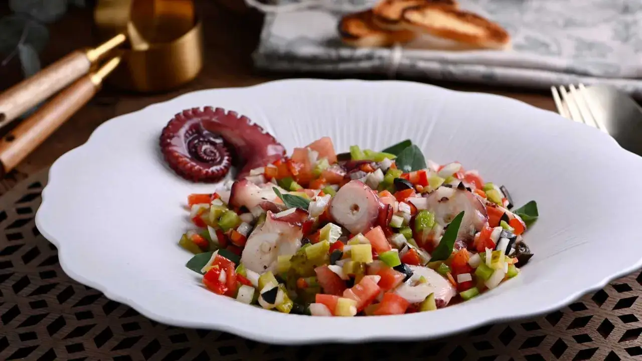 Salpicon de pulpo fresco con verduras picadas, servido en un plato blanco con un tent&aacute;culo de pulpo en espiral.