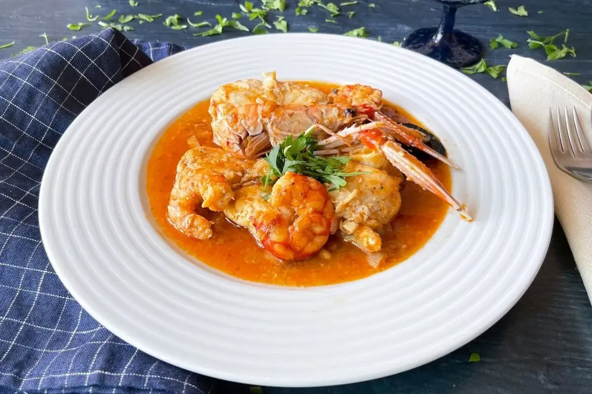 Rape a la marinera con gambas y cigalas, servido en plato blanco con perejil fresco.
