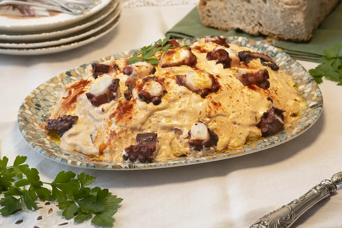 Deliciosa ensaladilla de pulpo cremosa, adornada con piment&oacute;n y perejil fresco, servida en un plato decorativo.