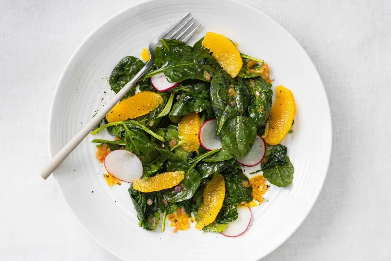 Ensalada de espinacas fresca con gajos de naranja, r&aacute;bano y un tenedor plateado.