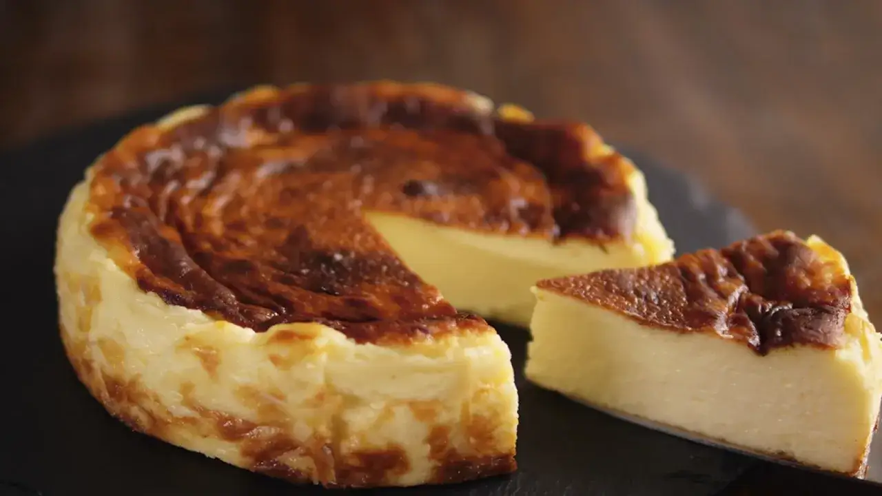 Tarta de queso con corteza dorada y cremosa textura interior. Una porción lista para disfrutar.