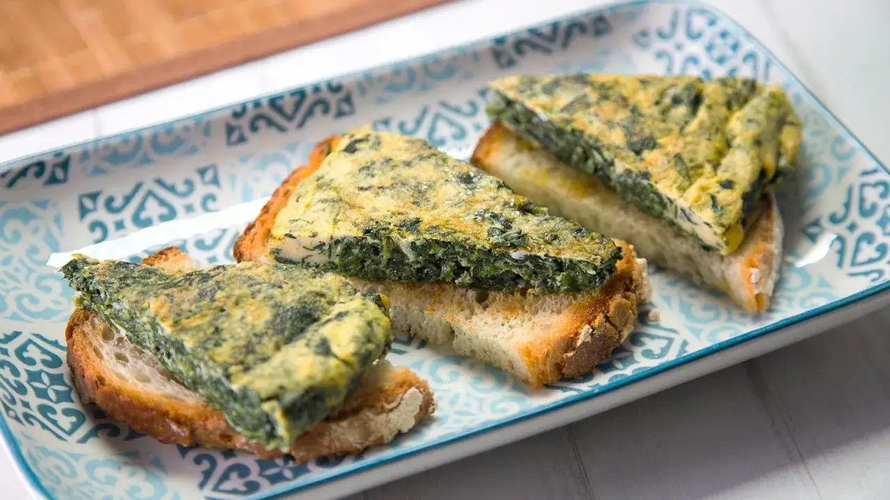 Rebanadas de pan tostado con una generosa porci&oacute;n de tortilla de espinacas encima, servidas en un plato decorado.