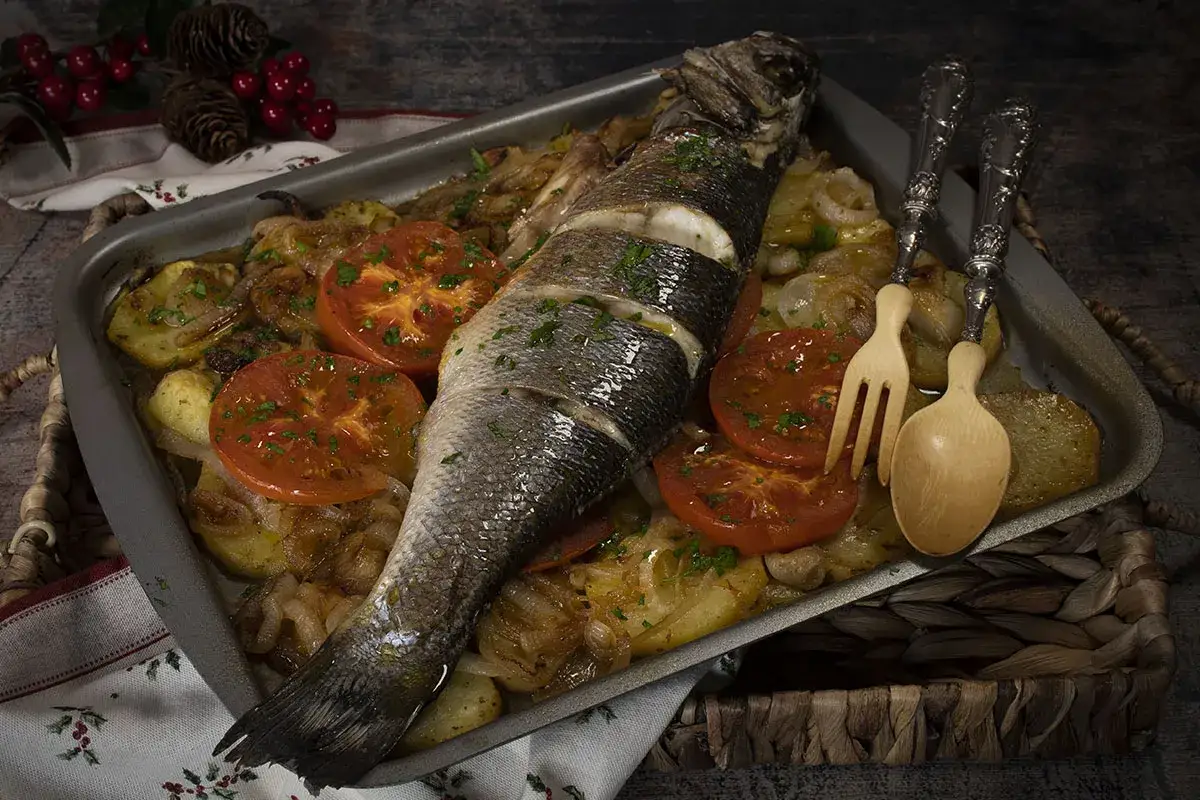 Lubina al horno con patatas, cebolla y tomates. Un plato principal delicioso y saludable, listo para servir.