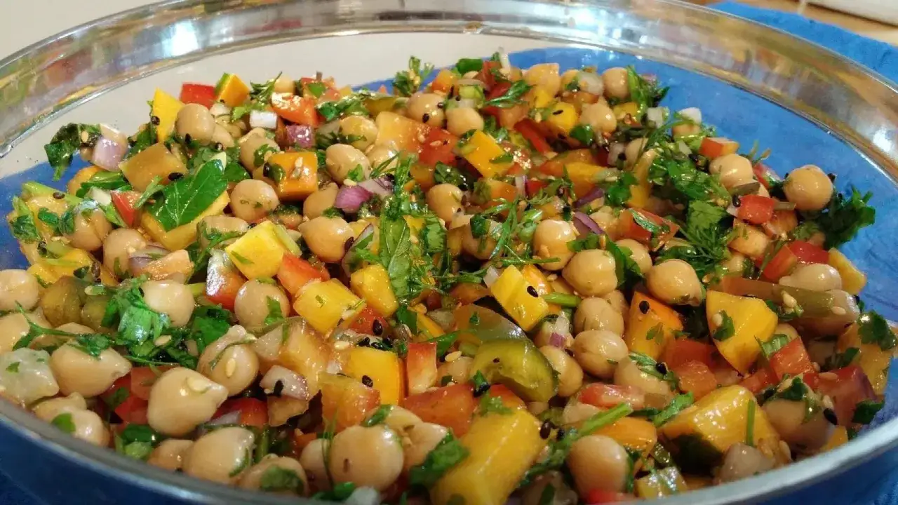 Ensalada de legumbres vibrante con garbanzos, pimientos, cebolla morada y cilantro fresco, todo mezclado en un taz&oacute;n de vidrio.