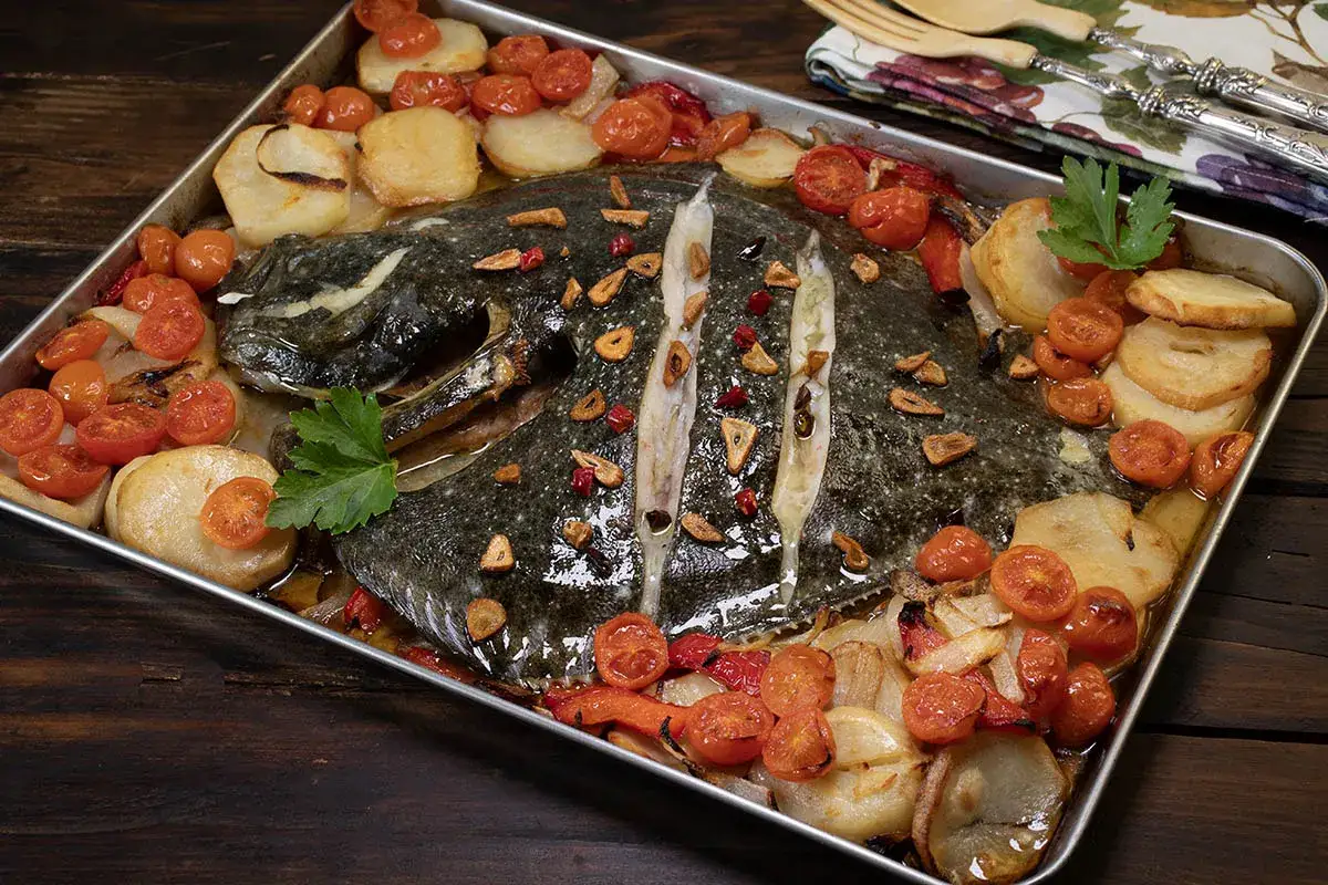 Rodaballo al horno con patatas, tomates cherry y ajo laminado, listo para servir.
