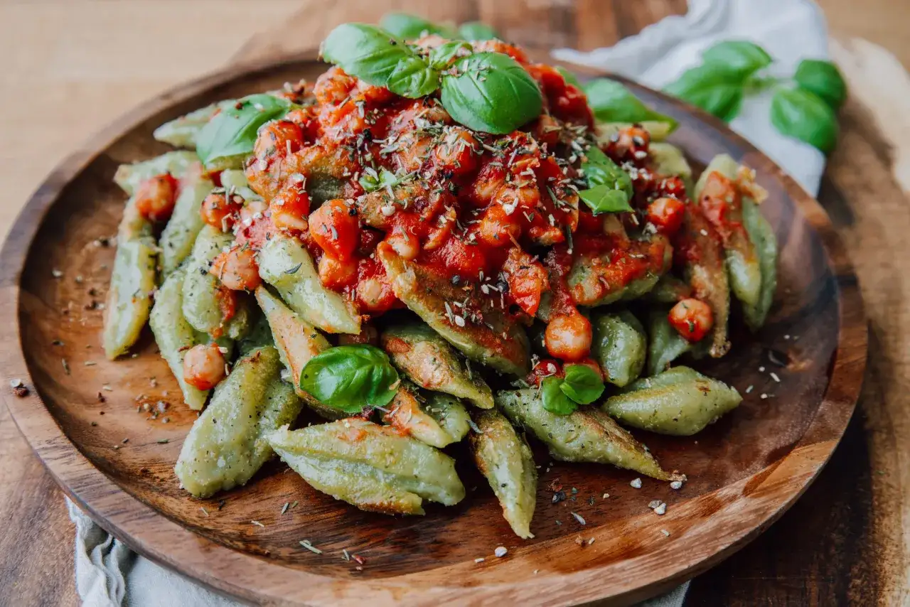 Pasta verde con br&oacute;coli, garbanzos y salsa de tomate, adornada con hojas de albahaca fresca.