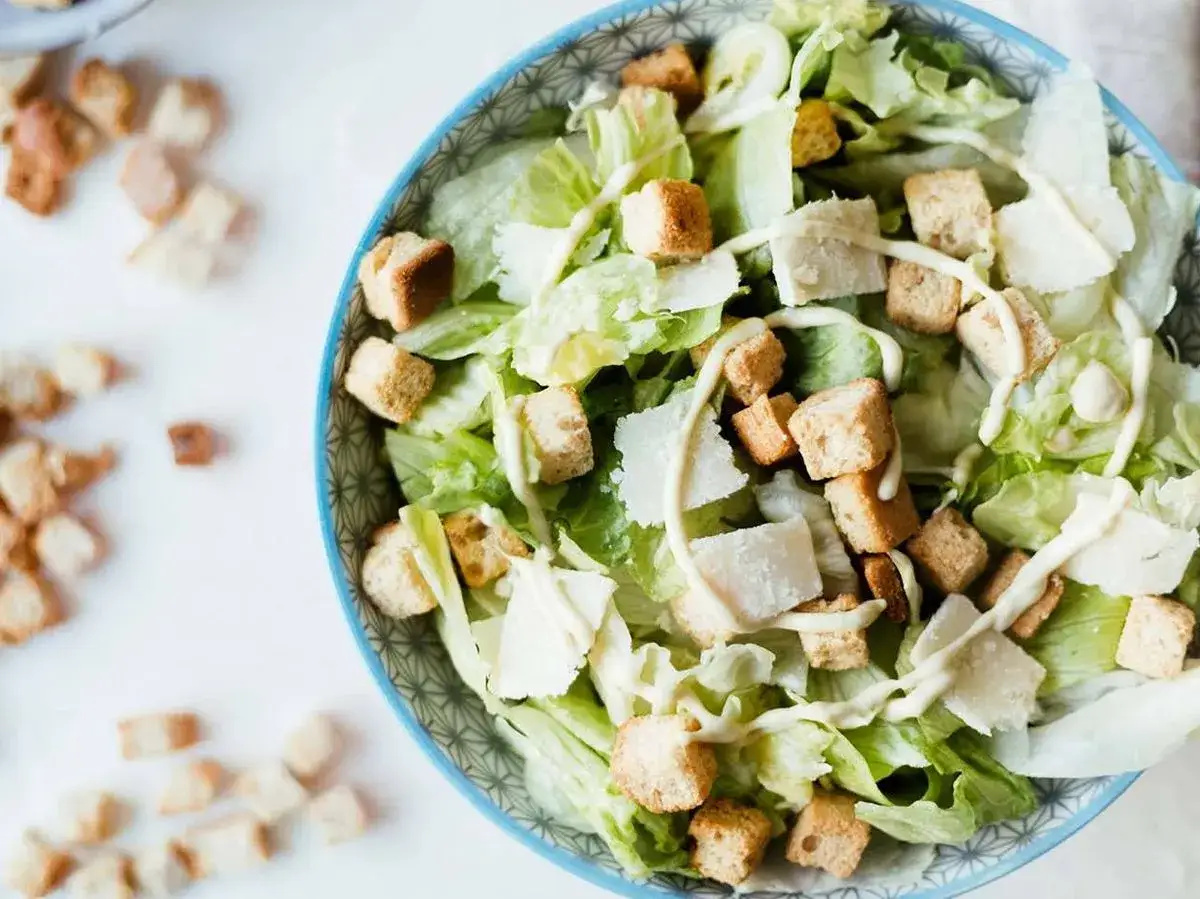Ensalada C&eacute;sar con lechuga, crutones dorados, l&aacute;minas de queso parmesano y aderezo cremoso. Ingredientes frescos para una ensalada cesar perfecta.
