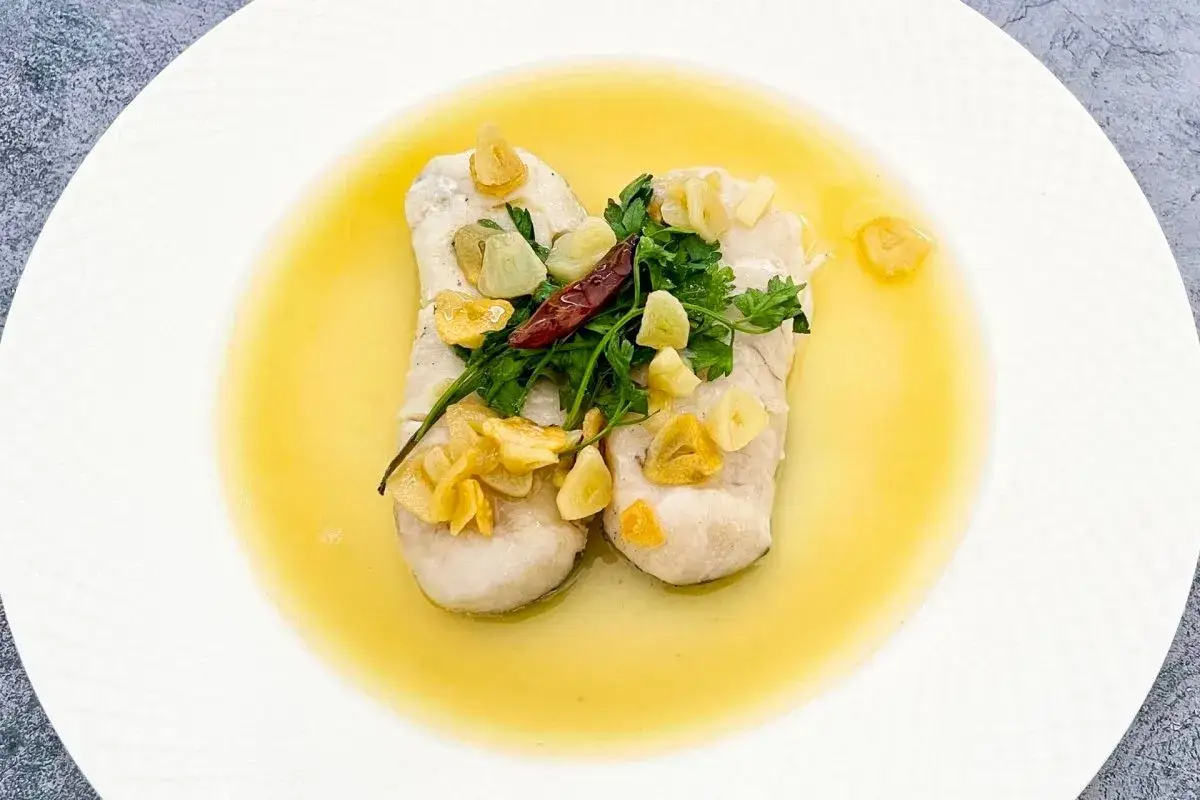 Dos lomos de merluza al pil pil, con láminas de ajo dorado, perejil fresco y un guindilla.