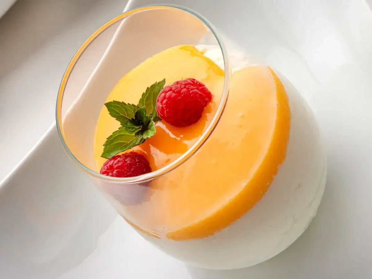 Delicioso postre en vaso: capas de tarta de chocolate blanco, crema de mango y frambuesas frescas con menta.