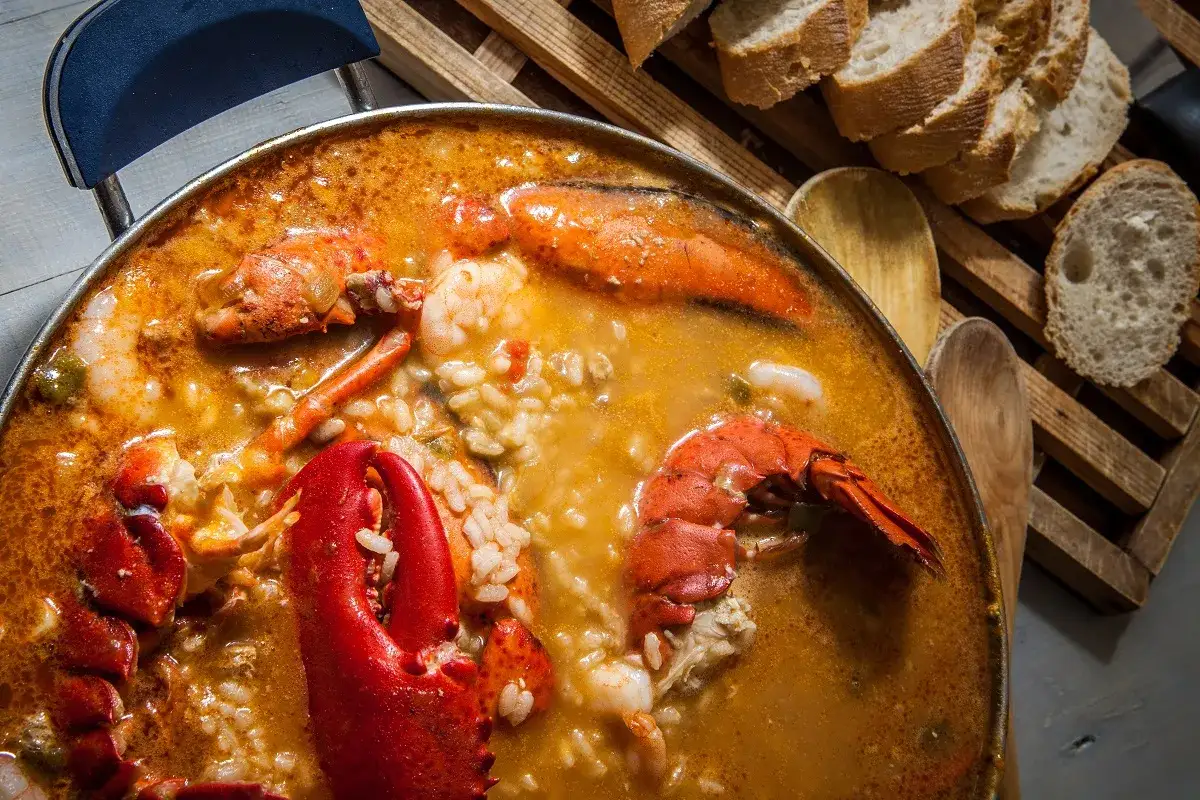 Arroz con bogavante humeante, con trozos de langosta y gambas, servido en una paellera.