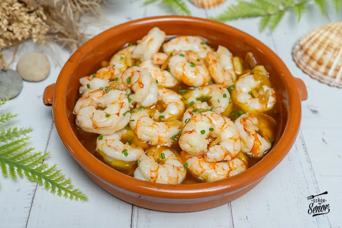 Gambones al ajillo burbujeantes en cazuela de barro, decorados con cebollino fresco. &iexcl;Un cl&aacute;sico irresistible!