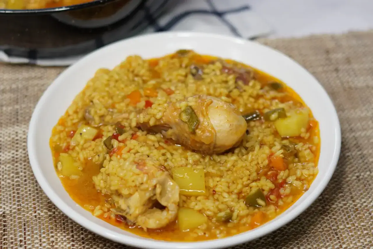 Delicioso arroz caldoso de marisco con trozos de pollo y verduras, servido en un plato blanco.