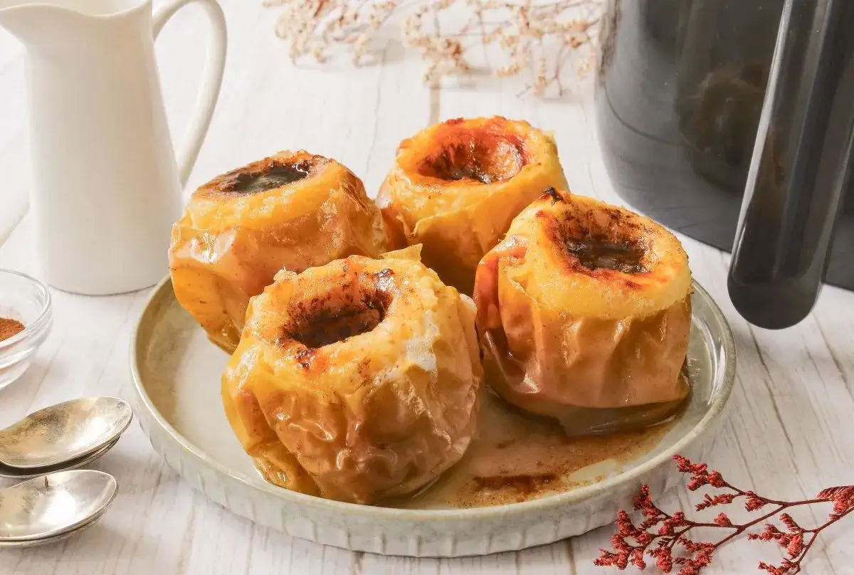 Cuatro manzanas asadas en freidora de aire, con el centro relleno de canela y az&uacute;car, servidas en un plato.