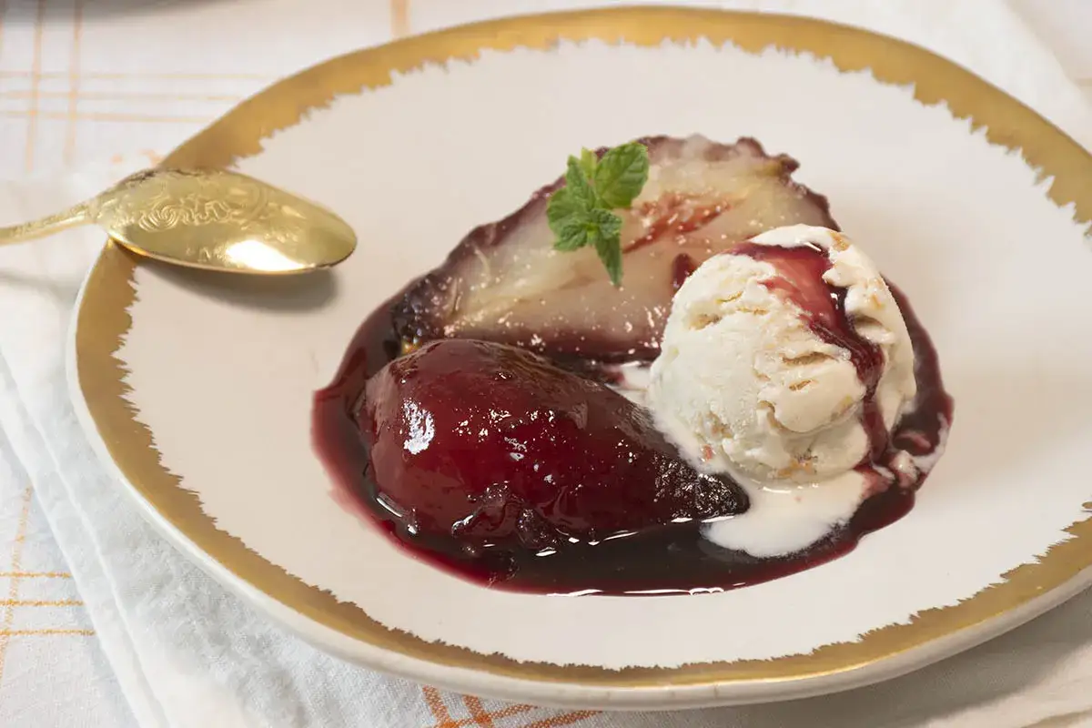 Peras al vino, tiernas y jugosas, ba&ntilde;adas en su sirope oscuro, acompa&ntilde;adas de una bola de helado cremoso y una hoja de menta.