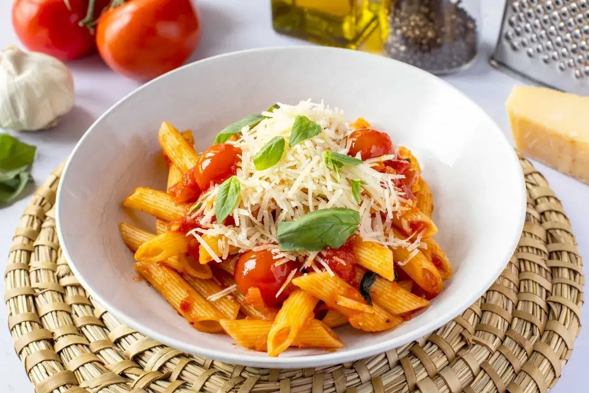 Un plato de macarrones a la napolitana con tomates frescos, albahaca y queso rallado.