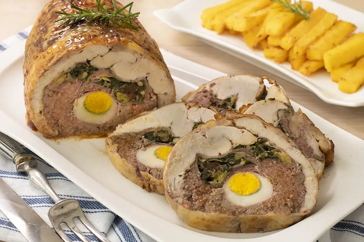 Roti de pollo relleno con huevo duro y verduras, servido en una bandeja blanca con papas fritas al fondo.