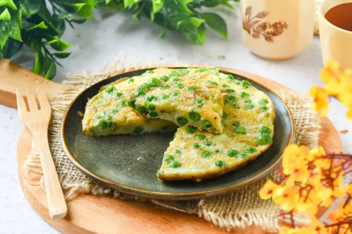 Tortilla de guisantes recién hecha, con trozos de patata y guisantes verdes, servida en un plato oscuro.