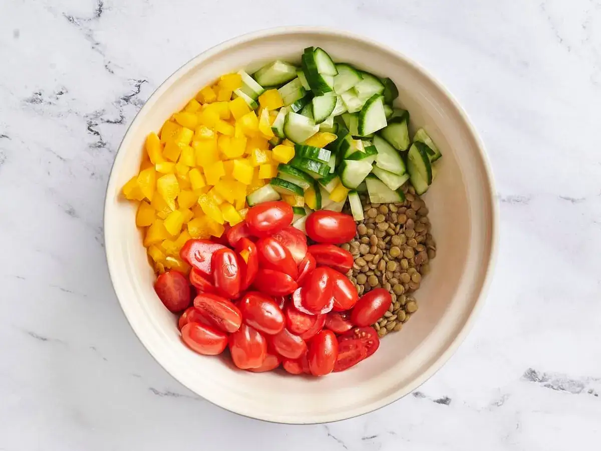Un taz&oacute;n con ingredientes para una ensalada de lentejas de bote: lentejas, tomates cherry, pimiento amarillo y pepino picados.