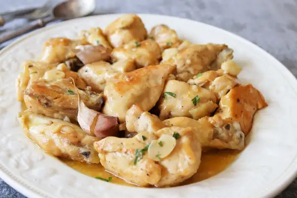 Sabroso pollo al ajillo servido en un plato blanco, con trozos de pollo dorados y dientes de ajo enteros.