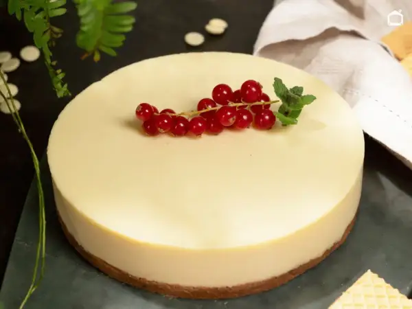 Deliciosa tarta de chocolate blanco, coronada con grosellas rojas y menta fresca. Un postre elegante y cremoso.