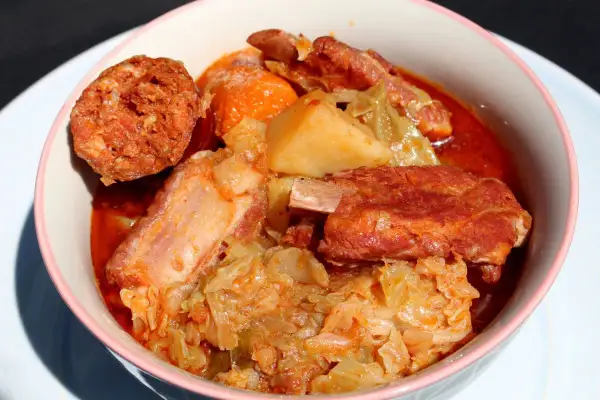 Un reconfortante plato de patatas con costillas, repollo y chorizo en un cuenco rosa.